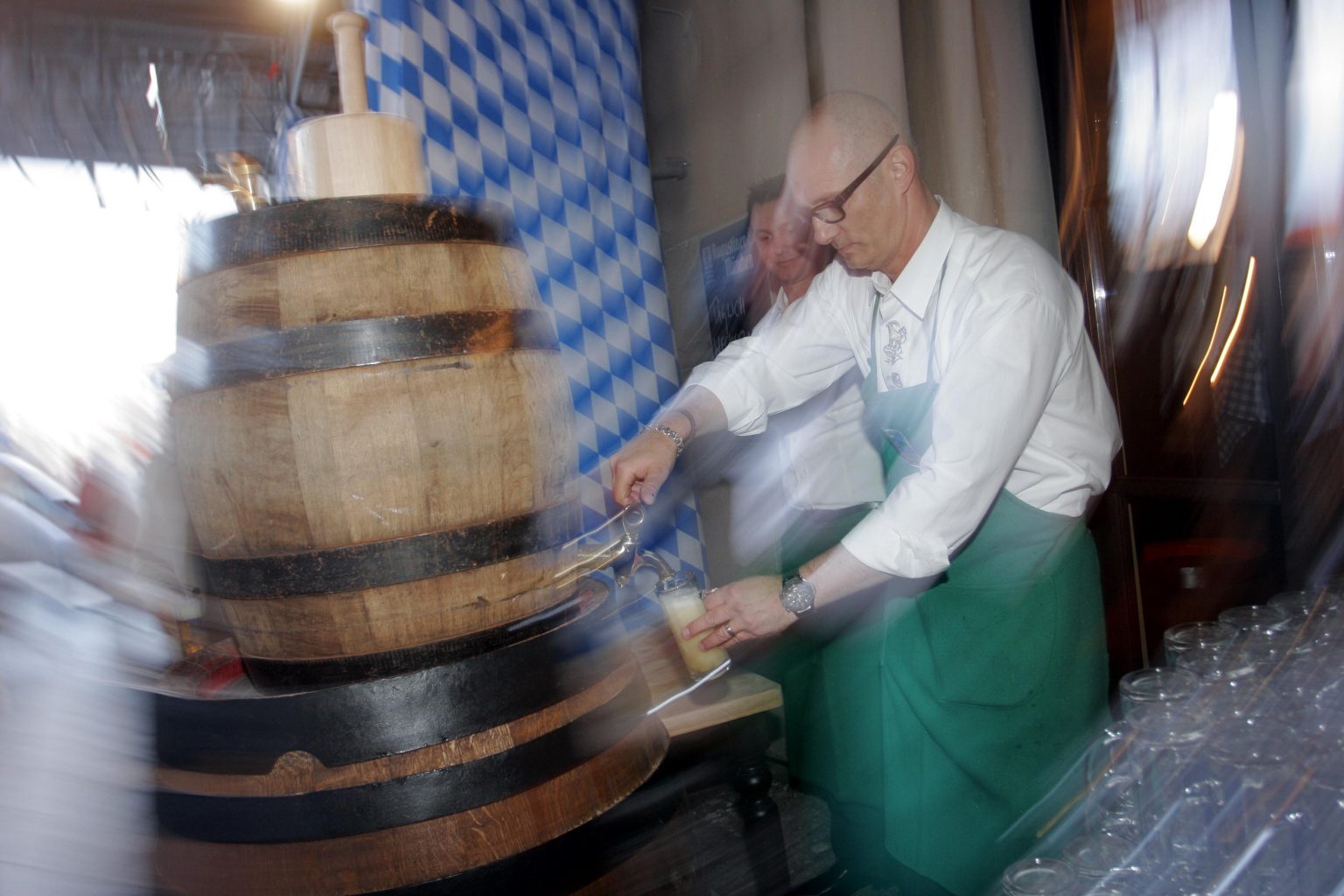 Ein Mitarbeiter bearbeitet die Oberfläche eines großen Holzfasses mit sichtbaren Metallreifen.