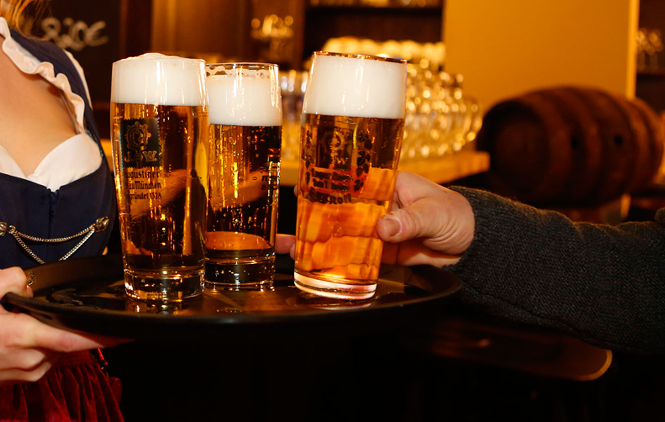 Servicekraft serviert mehrere frisch gezapfte Augustiner-Biere auf einem Tablett im Gastraum.