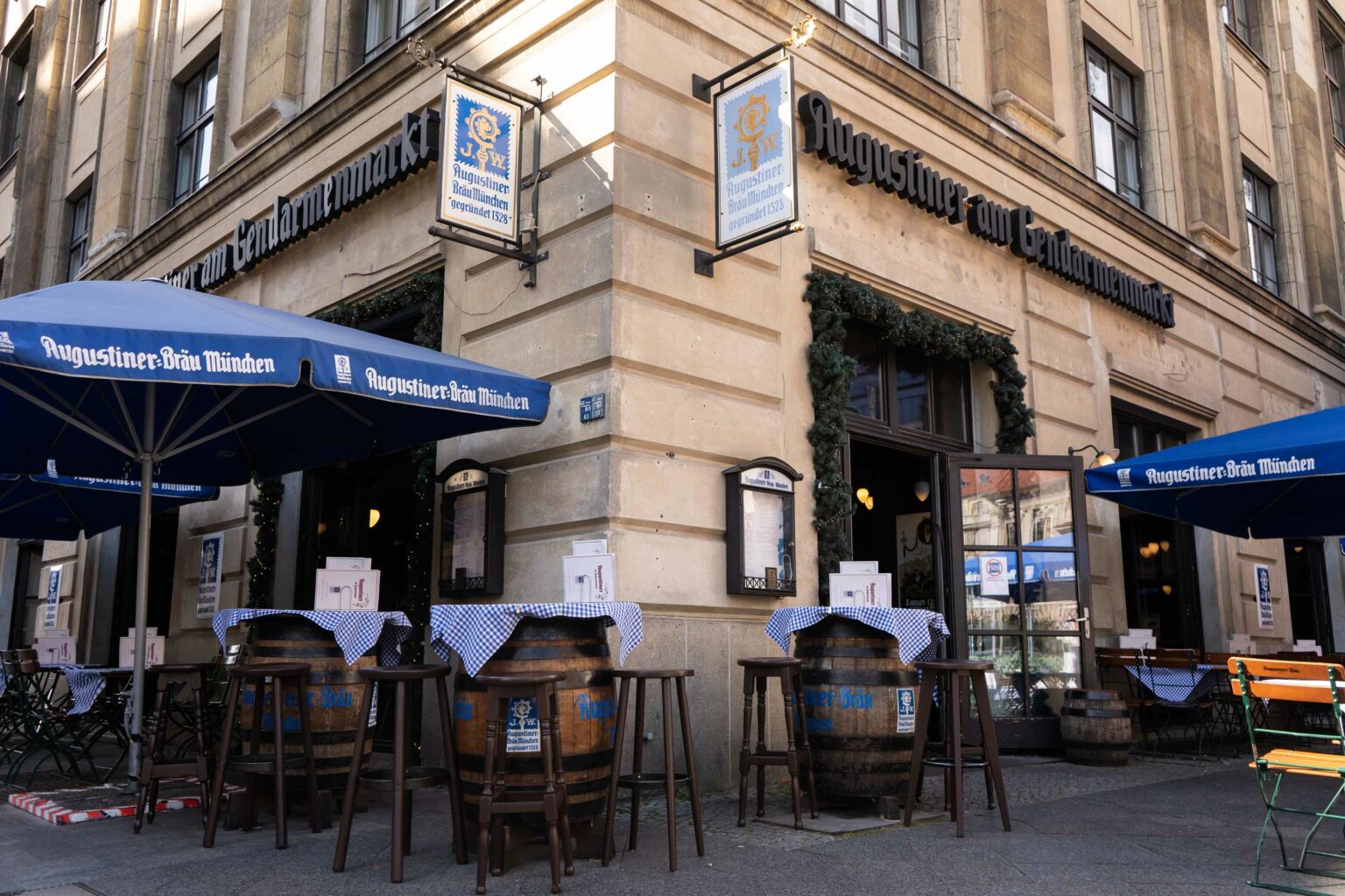 Außenansicht des Augustiner am Gendarmenmarkt mit Biergarten-Terrasse und blauen Sonnenschirmen.